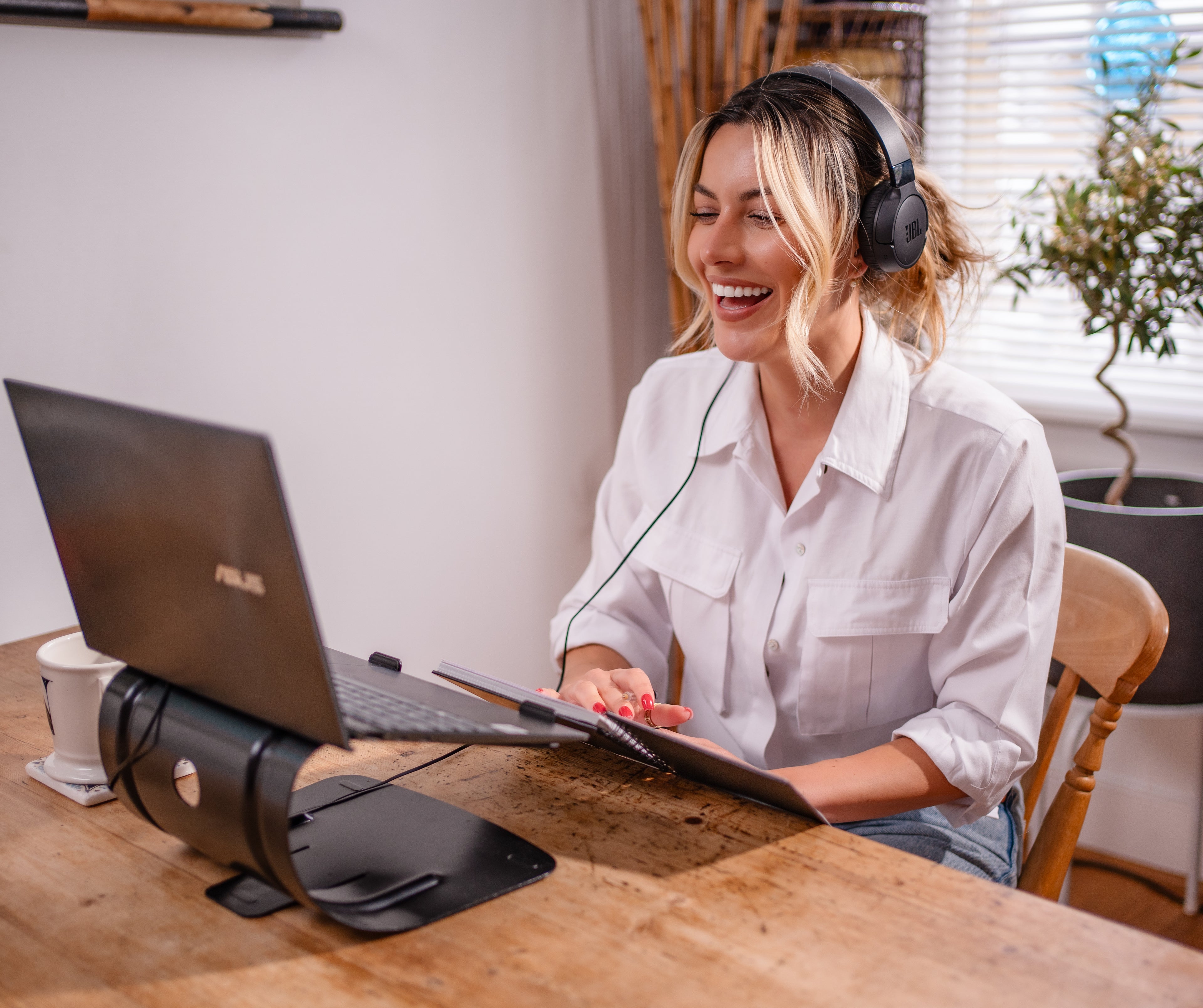 Woman wearing headphones and using a laptop at a wooden table.