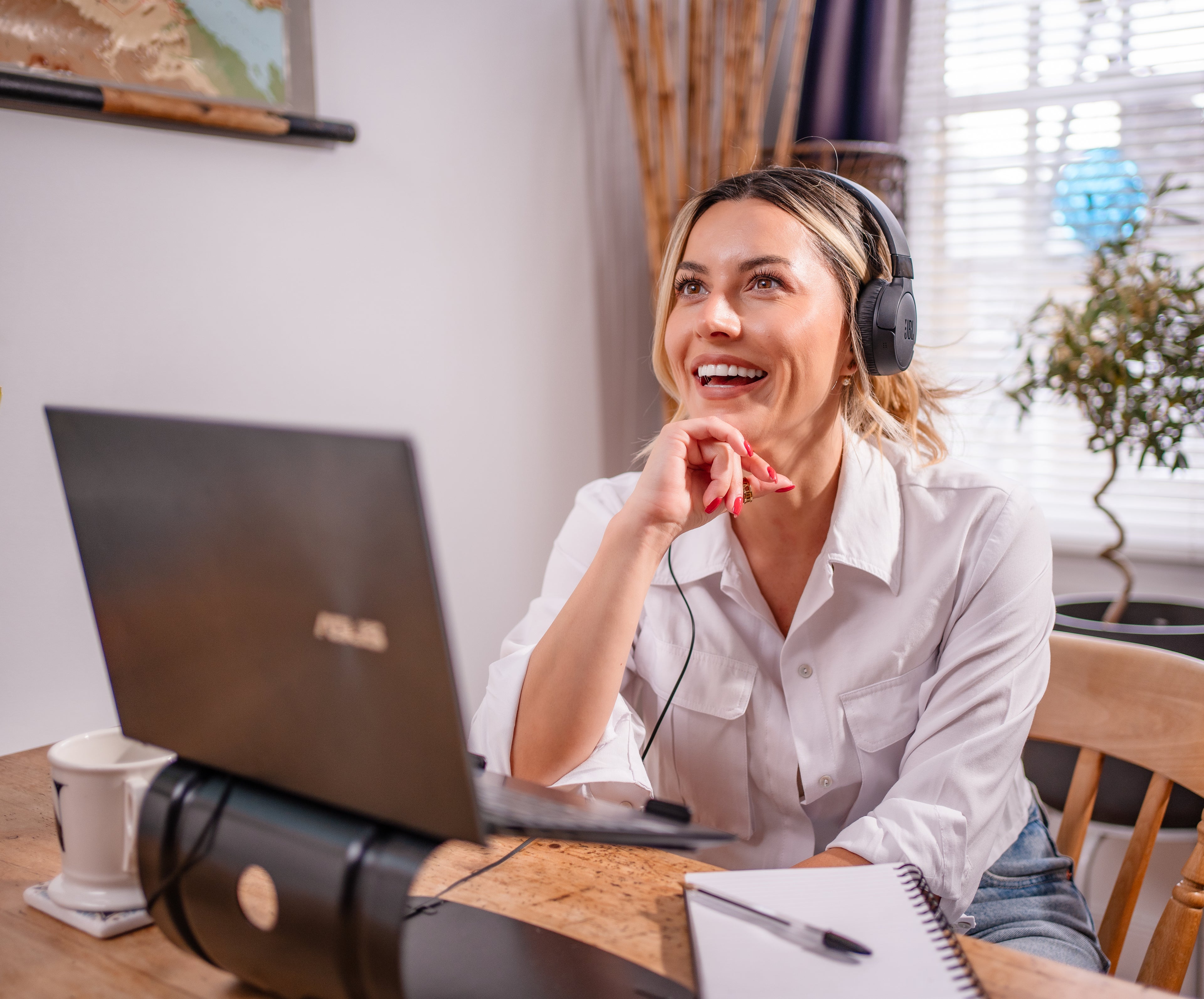 Woman wearing headphones and smiling while using a laptop at a desk.