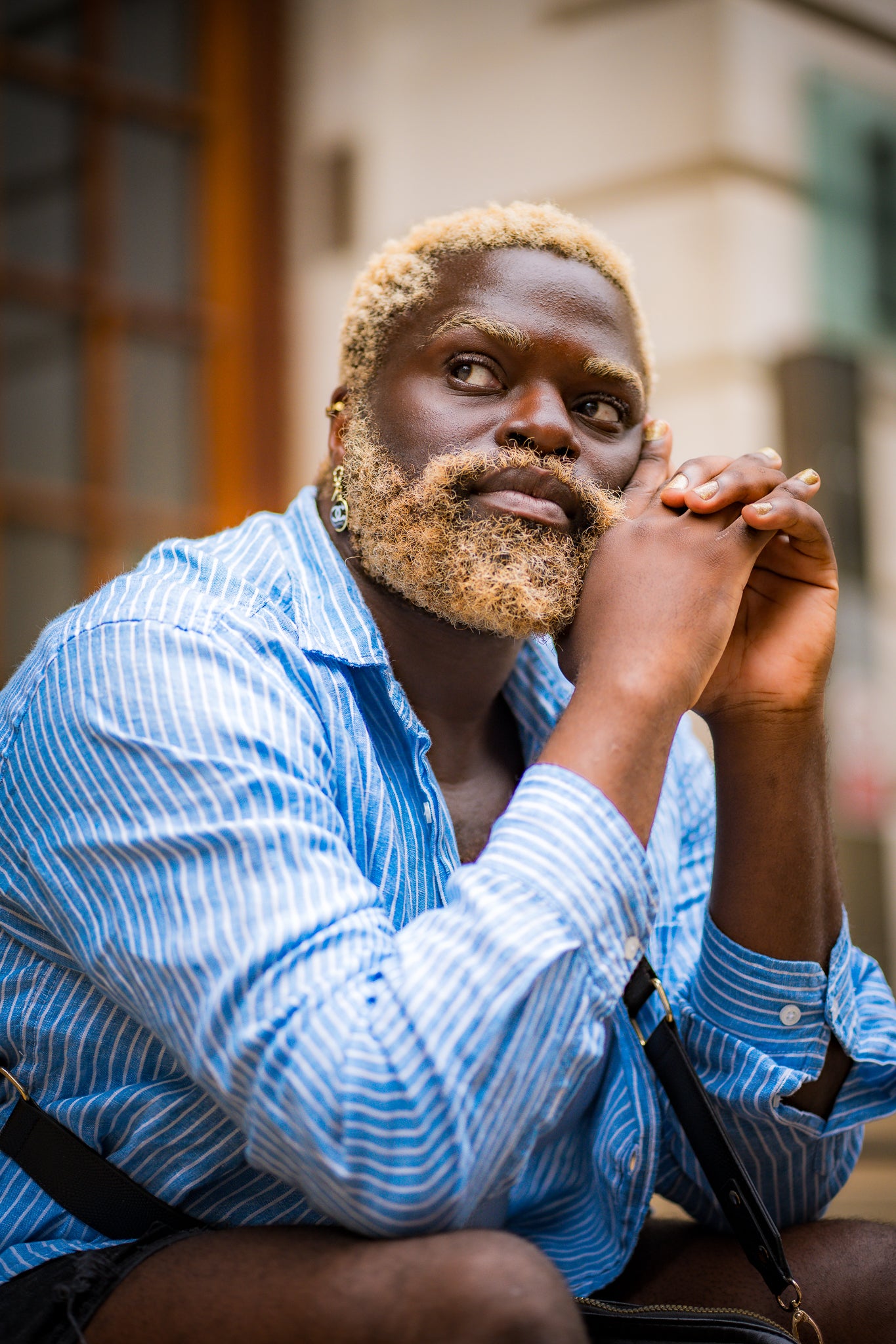 Man with blonde hair and beard wearing a blue striped shirt sitting outdoors.