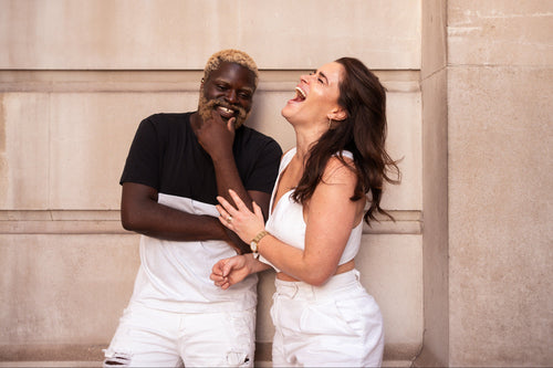 Two people laughing against a stone wall.