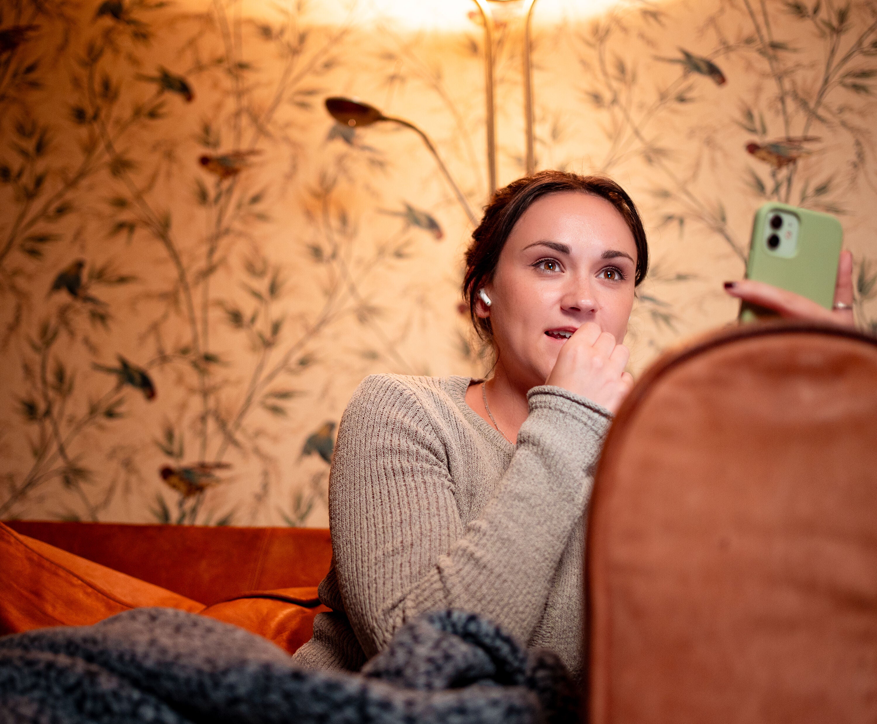 Woman sitting on a couch holding a phone with floral wallpaper in the background